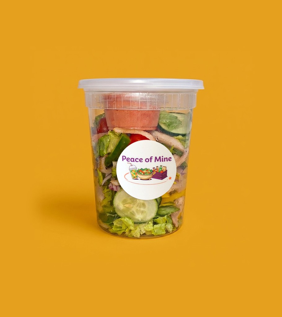 A Peace of Mine side salad in a to-go cup with dressing on top
